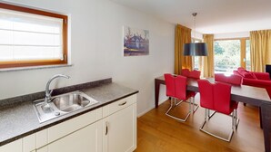 A modern kitchen with a sink and countertop, a dining area with red chairs, and a large window with curtains. - Walensee House & Apartments, (Unterterzen), by Interhome (Unterterzen)