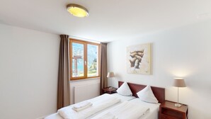 A hotel room with a bed, two bedside tables, a window with curtains, a painting on the wall, and a ceiling light. - Walensee House & Apartments, (Unterterzen), by Interhome (Unterterzen)