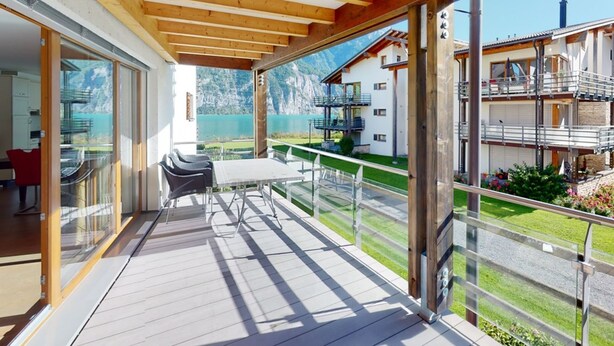 A wooden deck with a table and chairs, a glass door leading to a room, and a view of a mountain and lake. - Walensee House & Apartments, (Unterterzen), by Interhome (Unterterzen)