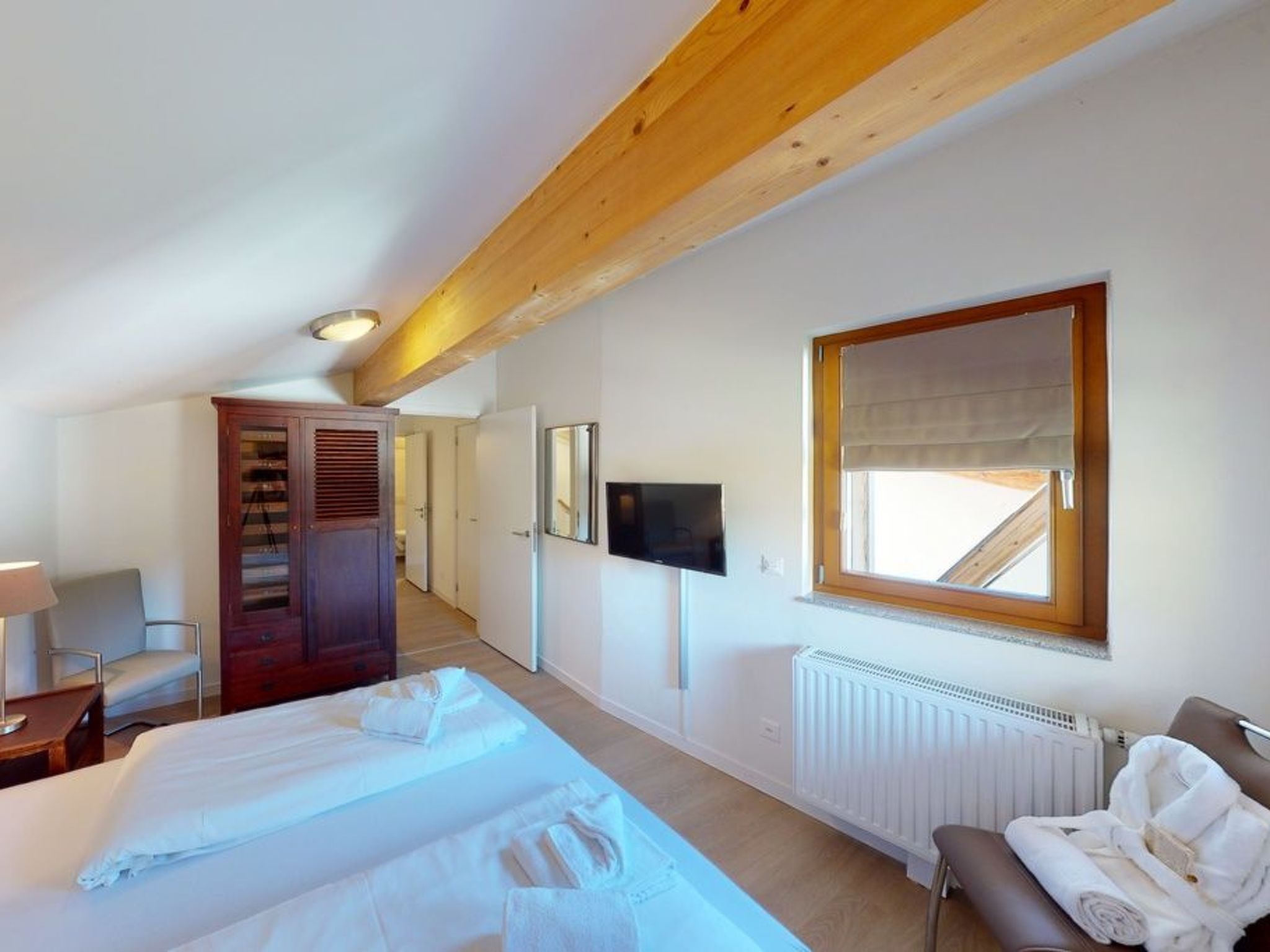 Une chambre d’hôtel avec un grand lit, une télévision, une fenêtre donnant sur un beau paysage, un plafond en bois et un radiateur.
