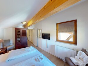 A hotel room with a large bed, a television, a window with a view, a wooden ceiling, and a radiator.