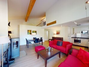 A modern living room with a red sofa, a wooden coffee table, and a dining area with a table and chairs.