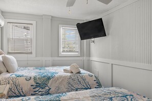 Ein Schlafzimmer mit einem Bett, einem Flachbildfernseher an der Wand und zwei Fenstern mit Jalousien.