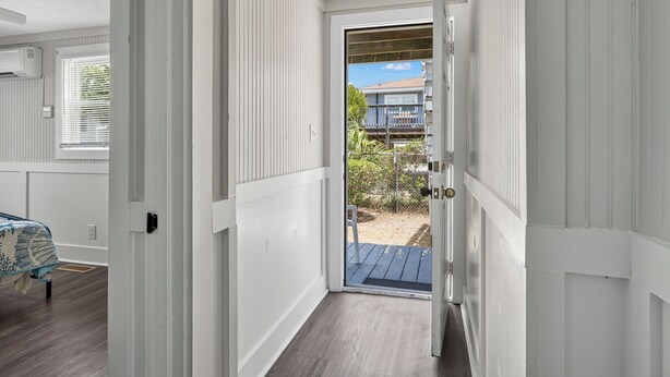A narrow hallway leading to a door with a view of a balcony and outdoor area.