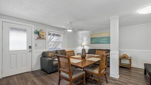 A dining area with a wooden table and chairs, a ceiling fan, and a painting on the wall.