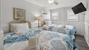 A bedroom with two beds, a ceiling fan, an air conditioning unit, a framed picture, and a mounted television.