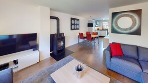 Una sala de estar moderna con televisor de pantalla plana, chimenea, comedor con sillas rojas y un sofá con almohada roja.