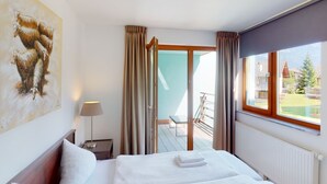 Habitación de hotel con cama, un cuadro, una lámpara, ventana con vistas y puerta corredera a un espacio exterior.