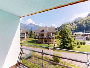 A residential building with a balcony, a lawn, and mountains in the background.