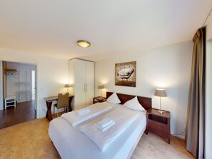 Una habitación de hotel con una cama grande, un escritorio, una silla, una mesita de noche y un cuadro en la pared.