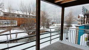 Un balcón con barandilla de metal, vista a un paisaje nevado y un edificio con fachada de madera.