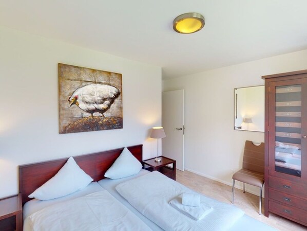 A hotel room with a bed, a nightstand, a lamp, a wooden cabinet, and a painting on the wall.