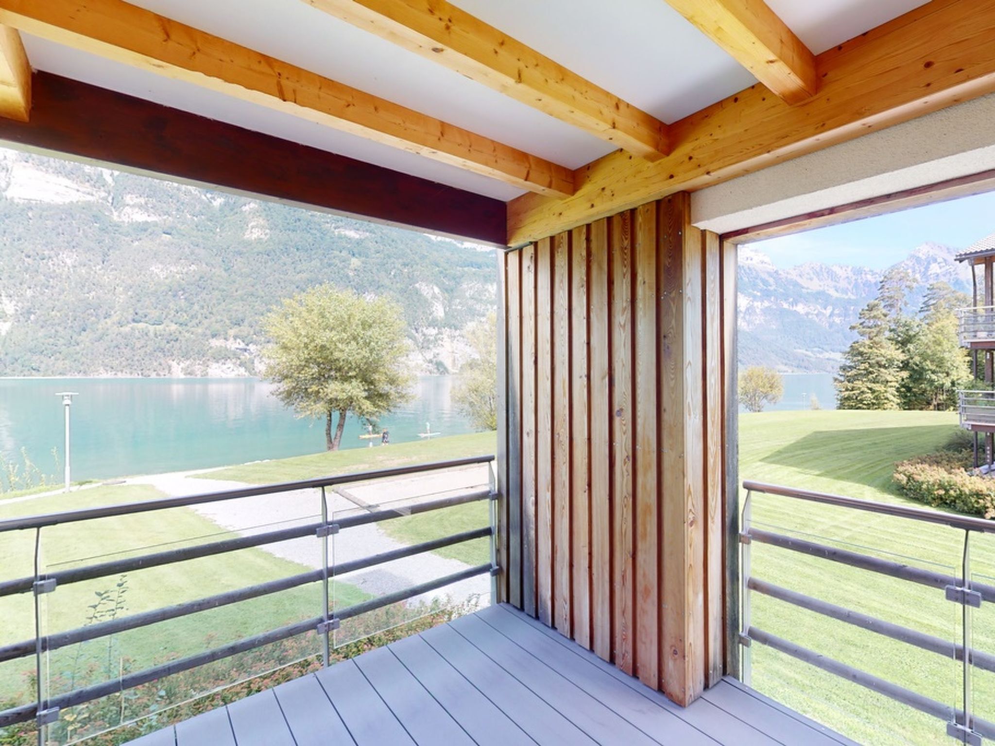 Un balcon avec vue sur un lac et des montagnes, des poutres en bois et une rambarde en métal.