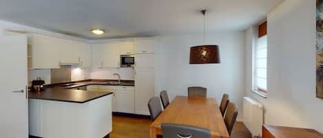 Eine moderne Küche mit weißen Schränken, einem Holztisch und einer Pendelleuchte.