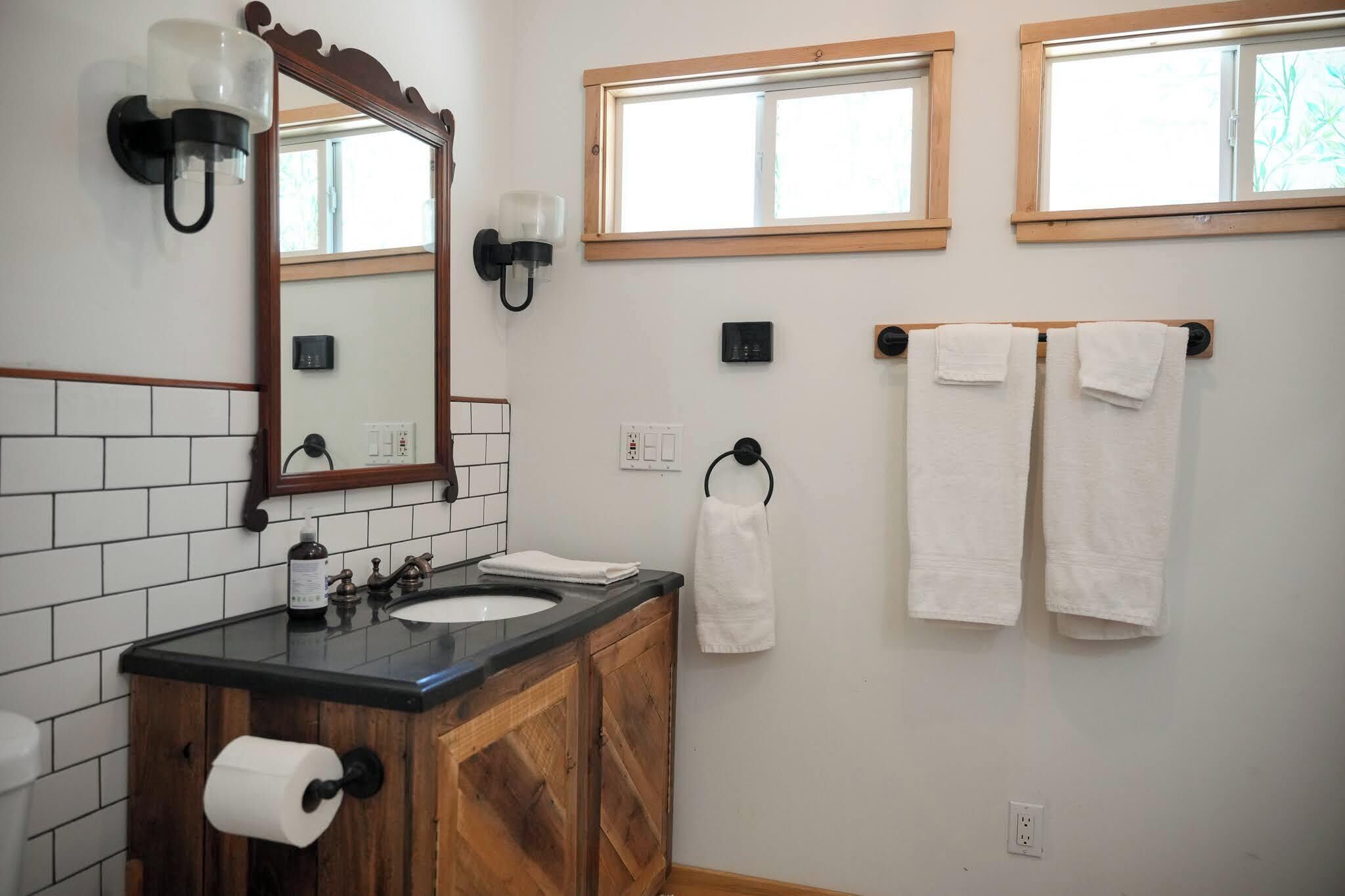 A bathroom with a wooden vanity, a mirror, two windows, and two towels hanging on a rack.
