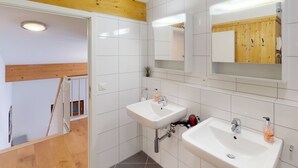 Ein modernes Badezimmer mit zwei Waschbecken, Holzbalkendecke und einem großen Spiegel.