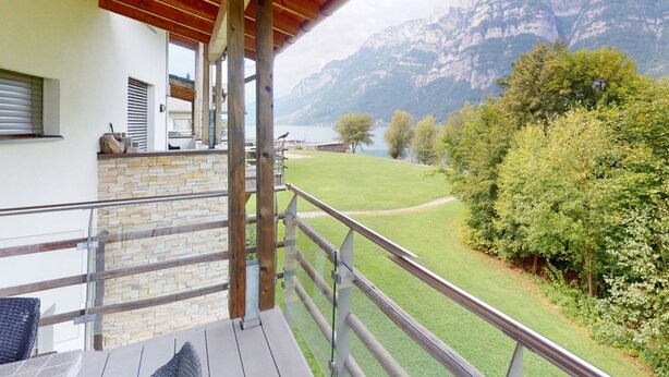 Ein Balkon mit Holzboden, Steinwand und Blick auf Berge und einen See.