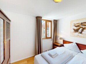 A hotel room with a bed, a nightstand, a lamp, a window with curtains, and a painting on the wall. - Walensee House & Apartments, (Unterterzen), by Interhome (Unterterzen)