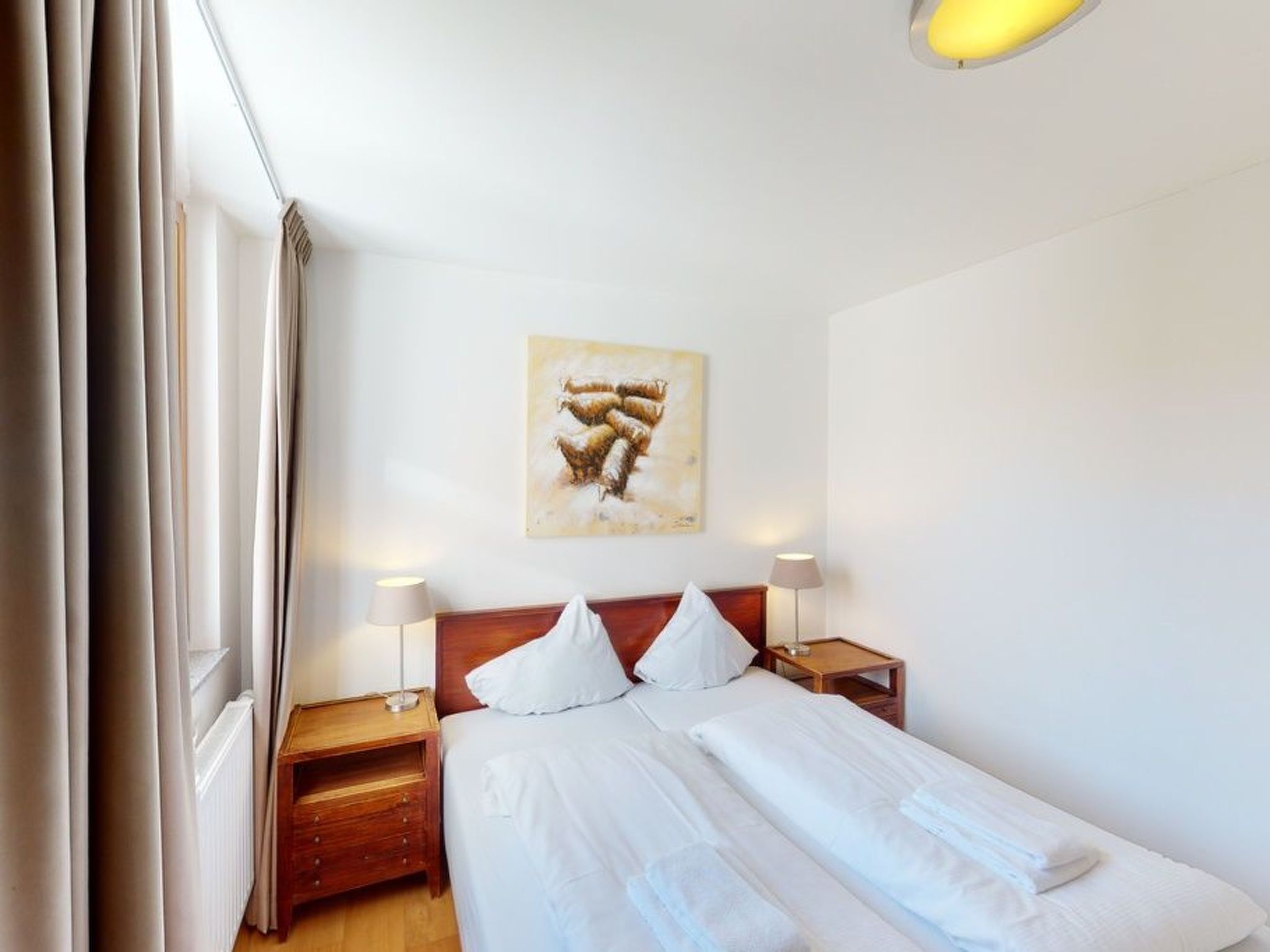 Ett hotellrum med en säng, två sängbord, en lampa och en tavla på väggen.