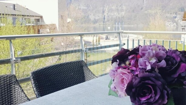 Ein Tisch mit einem Blumenstrauß, ein Stuhl und im Hintergrund Wasser sowie Gebäude.