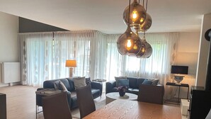 Ein modernes Wohnzimmer mit Essbereich, ausgestattet mit einem Holztisch, Sofas und einer einzigartigen Pendelleuchte.