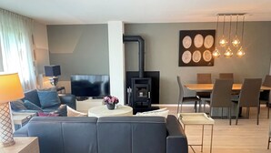 Ein modernes Wohnzimmer mit Sofa, Fernseher, Kamin, Essbereich und Pendelleuchten.