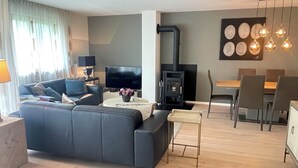 Ein modernes Wohnzimmer mit Sofa, Fernseher, Kamin, Essbereich und Pendelleuchten.