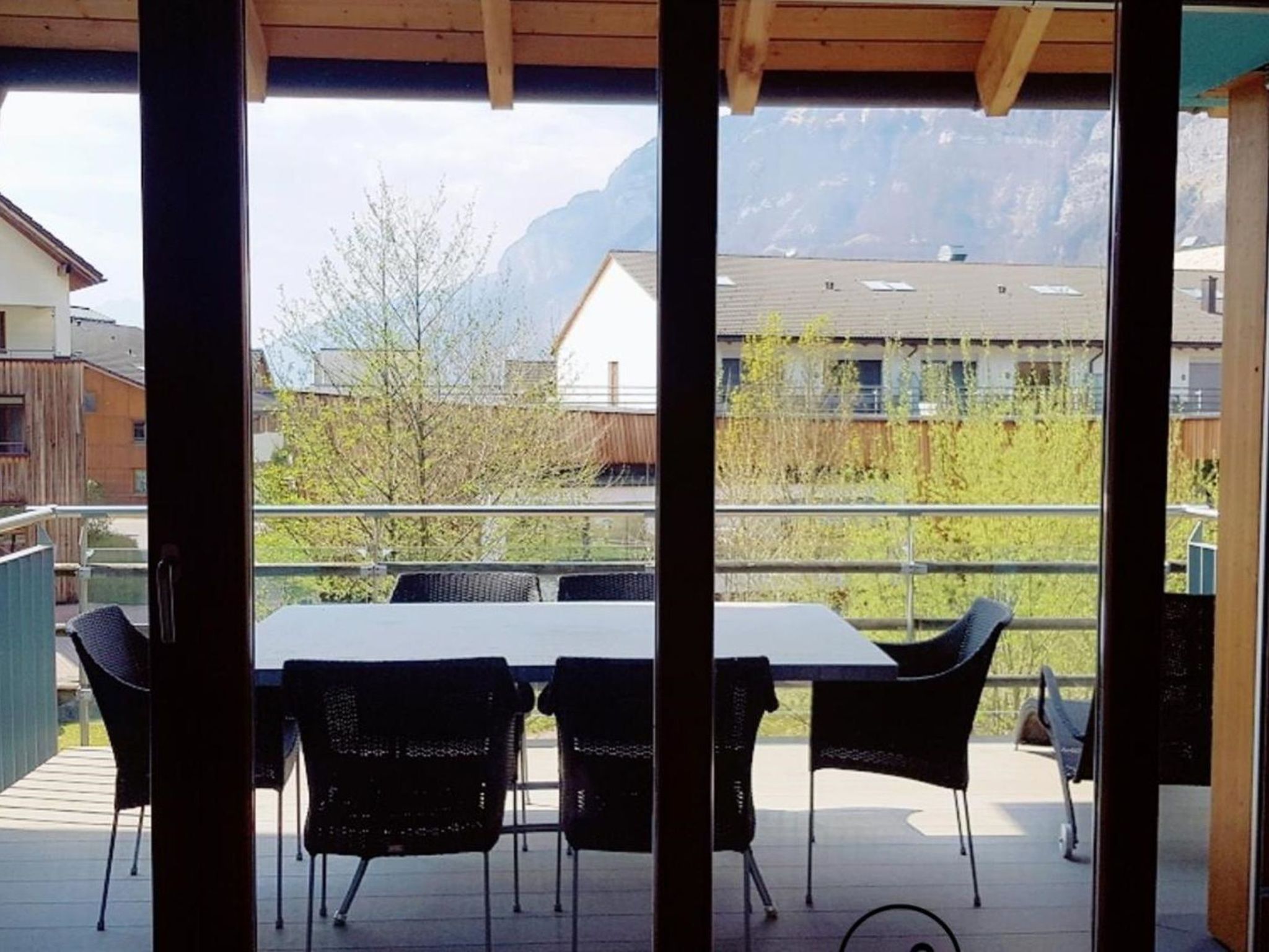A balcony with a table and chairs, overlooking a residential area with houses and mountains.