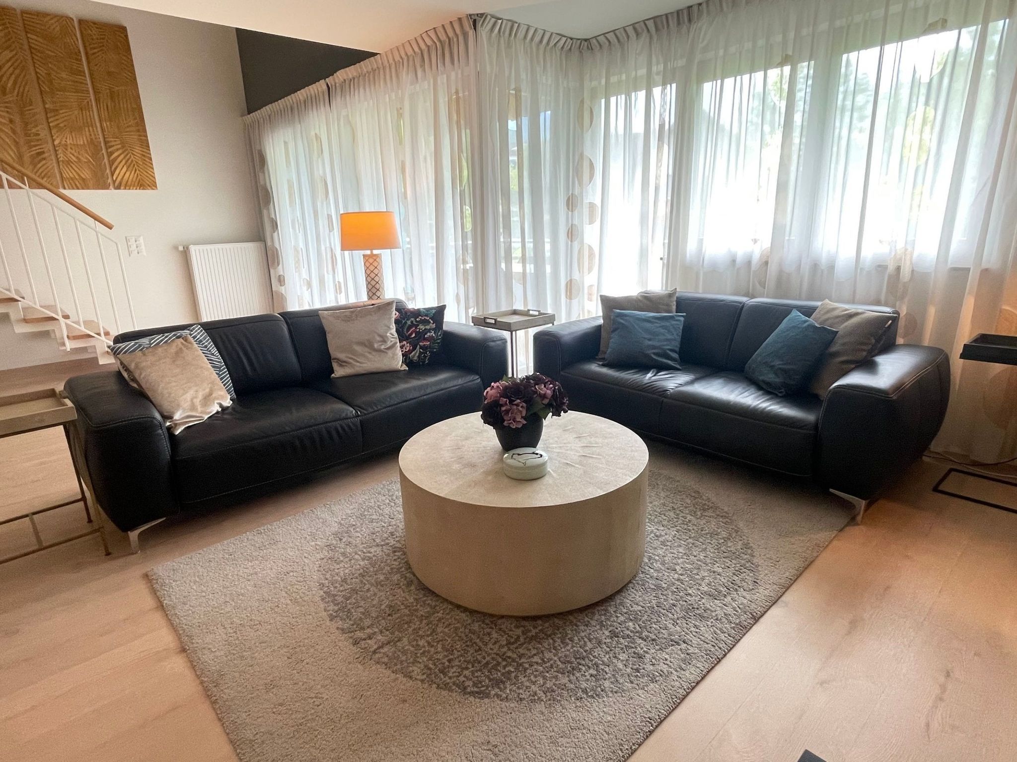 A living room with a sectional sofa, a round coffee table with a vase, and a lamp.