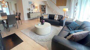 Ein modernes Wohnzimmer mit einer schwarzen Ledersofa, einem runden Couchtisch und einem Essbereich mit Holztisch und Stühlen.