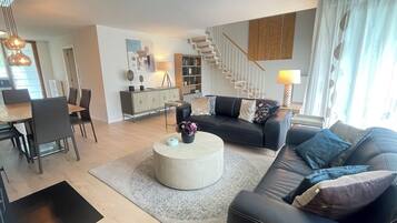 Un salon moderne avec un canapé en cuir noir, une table basse ronde et un coin repas comprenant une table et des chaises en bois.