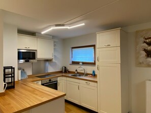 A modern kitchen with white cabinets, a wooden countertop, a built-in microwave, and a window above the sink.