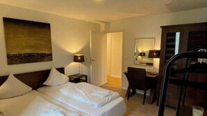 Quarto de hotel com cama, abajures, escrivaninha com cadeira, espelho e um quadro na parede.