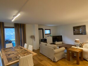 A modern living room with a sofa, a TV, a dining table, and a lamp.