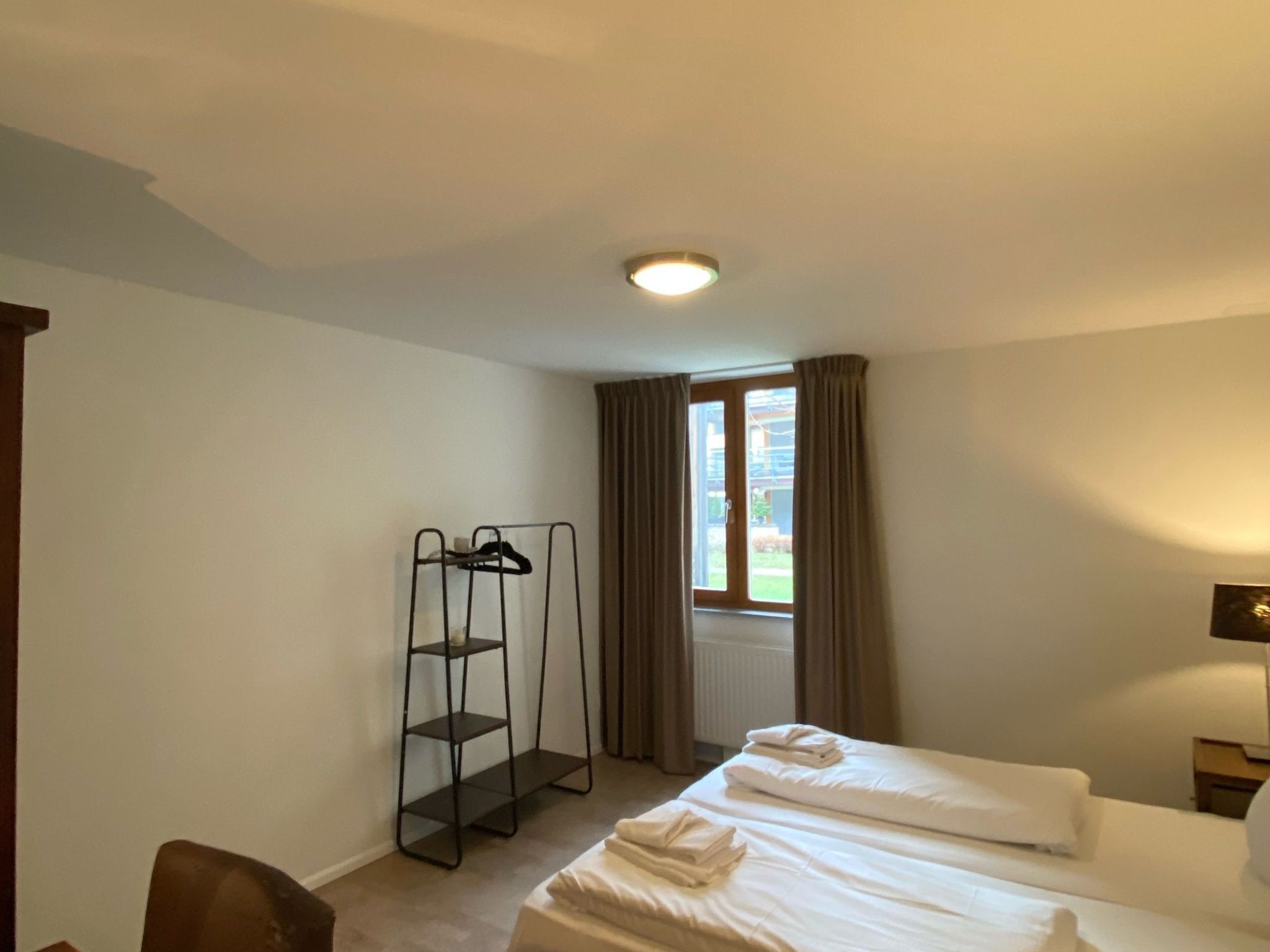 A hotel room with two beds, a wardrobe, a radiator, and a window with curtains.