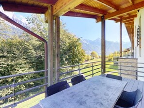 A covered outdoor seating area with a table and chairs, overlooking a mountainous landscape.