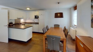 Een moderne keuken met witte kastjes, een centraal eiland en een eethoek met een houten tafel en stoelen.