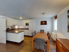 Eine moderne Küche mit weißen Schränken, einer zentralen Kochinsel und einem Essbereich mit einem Holztisch und Stühlen.
