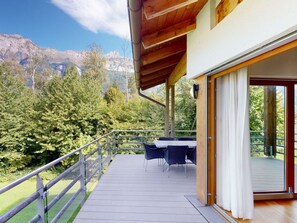 Um deck de madeira com mesa e cadeiras, com vista para uma paisagem montanhosa.