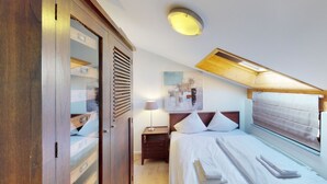 Een slaapkamer met een bed, nachtkastje, lamp, houten garderobe en dakraam.