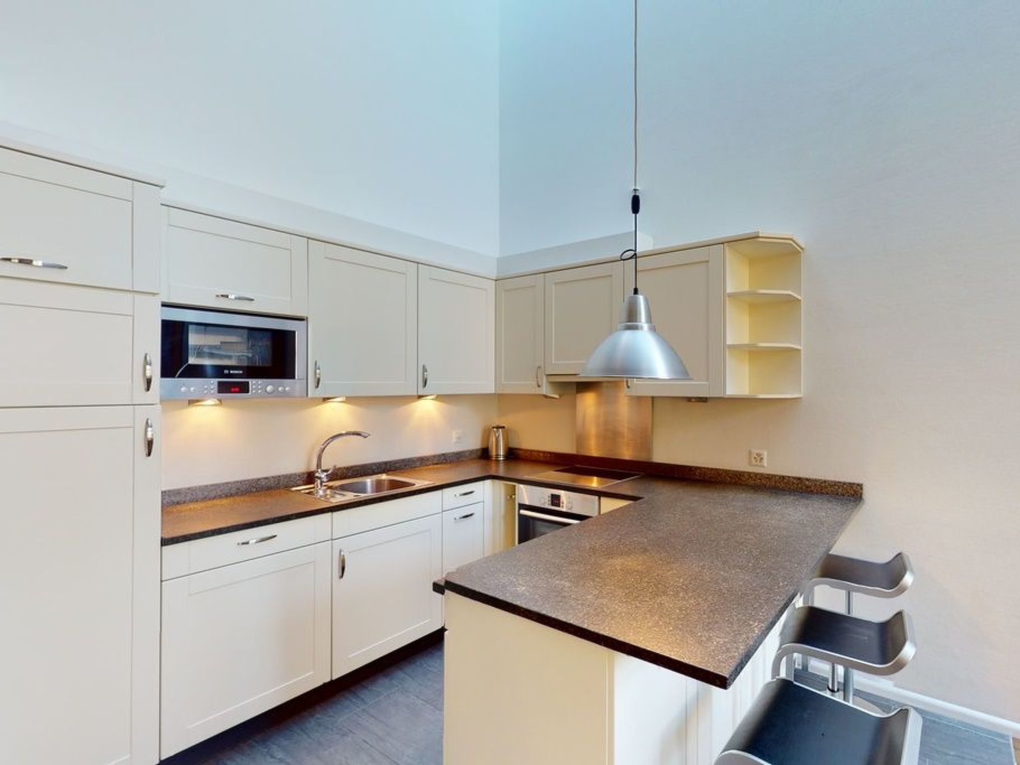 A modern kitchen with white cabinetry, a built-in microwave, a stainless steel sink, and a pendant light.