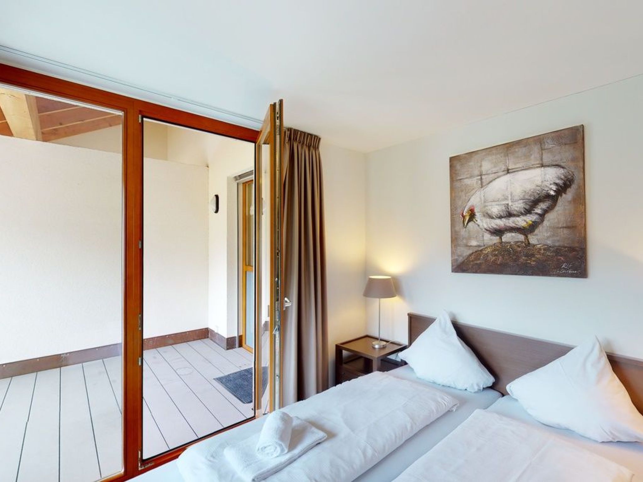 A hotel room with a bed, a nightstand, a lamp, a painting, and a sliding door leading to an outdoor area.