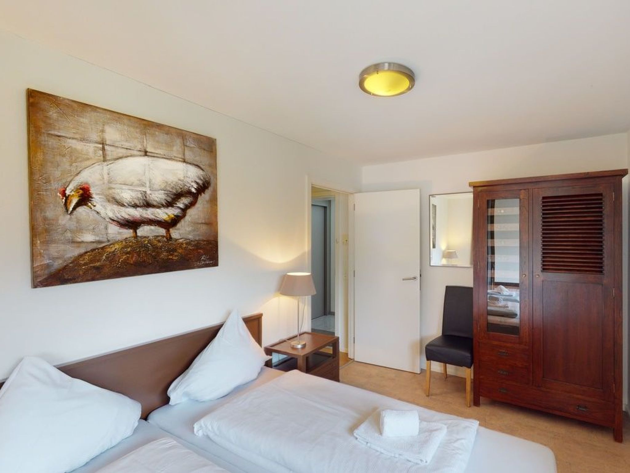 A hotel room with a bed, a wooden wardrobe, a painting, and a lamp.