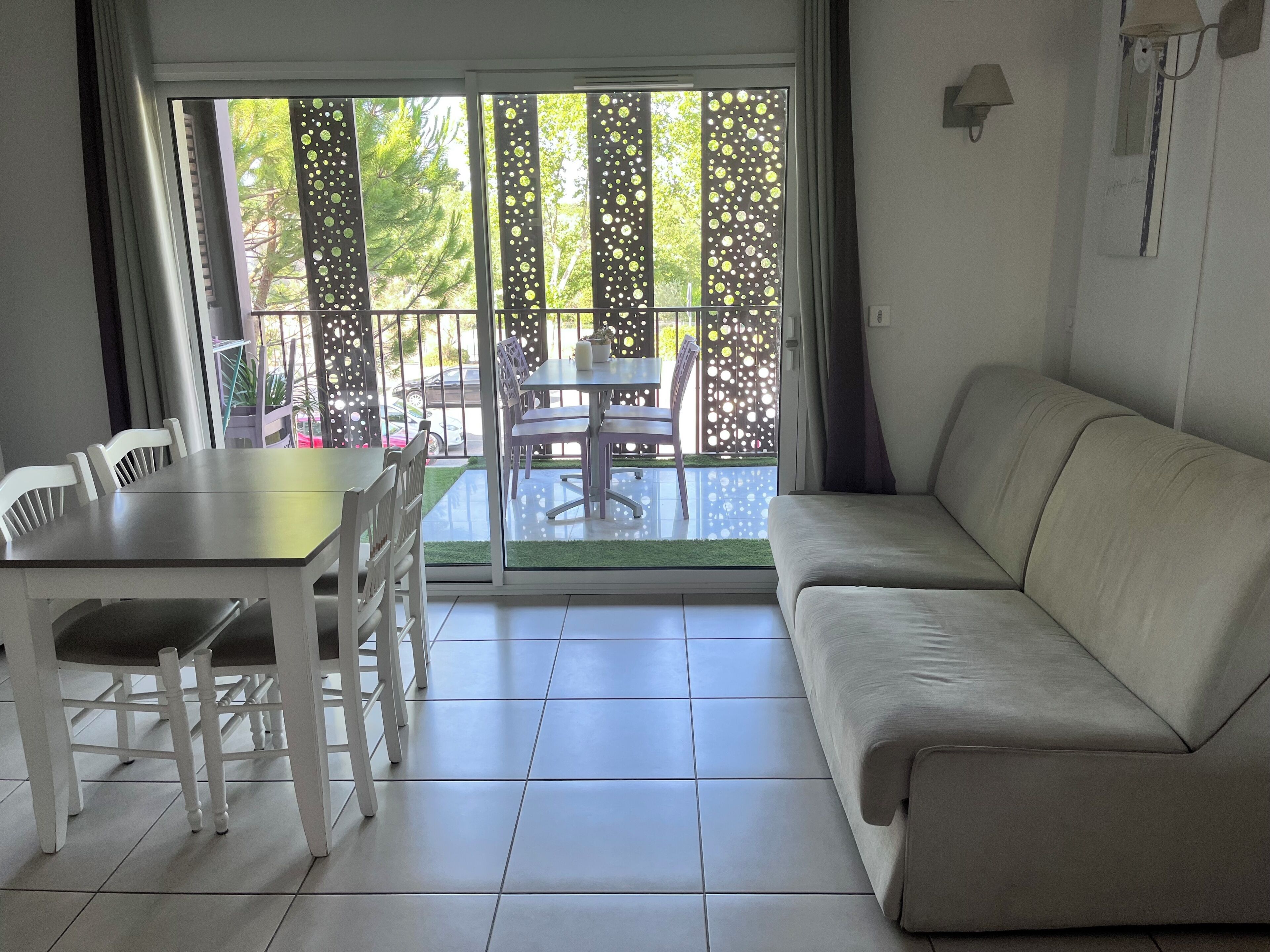 A living room with a sofa, a dining table with chairs, and a sliding glass door leading to an outdoor area with a patio table and chairs.