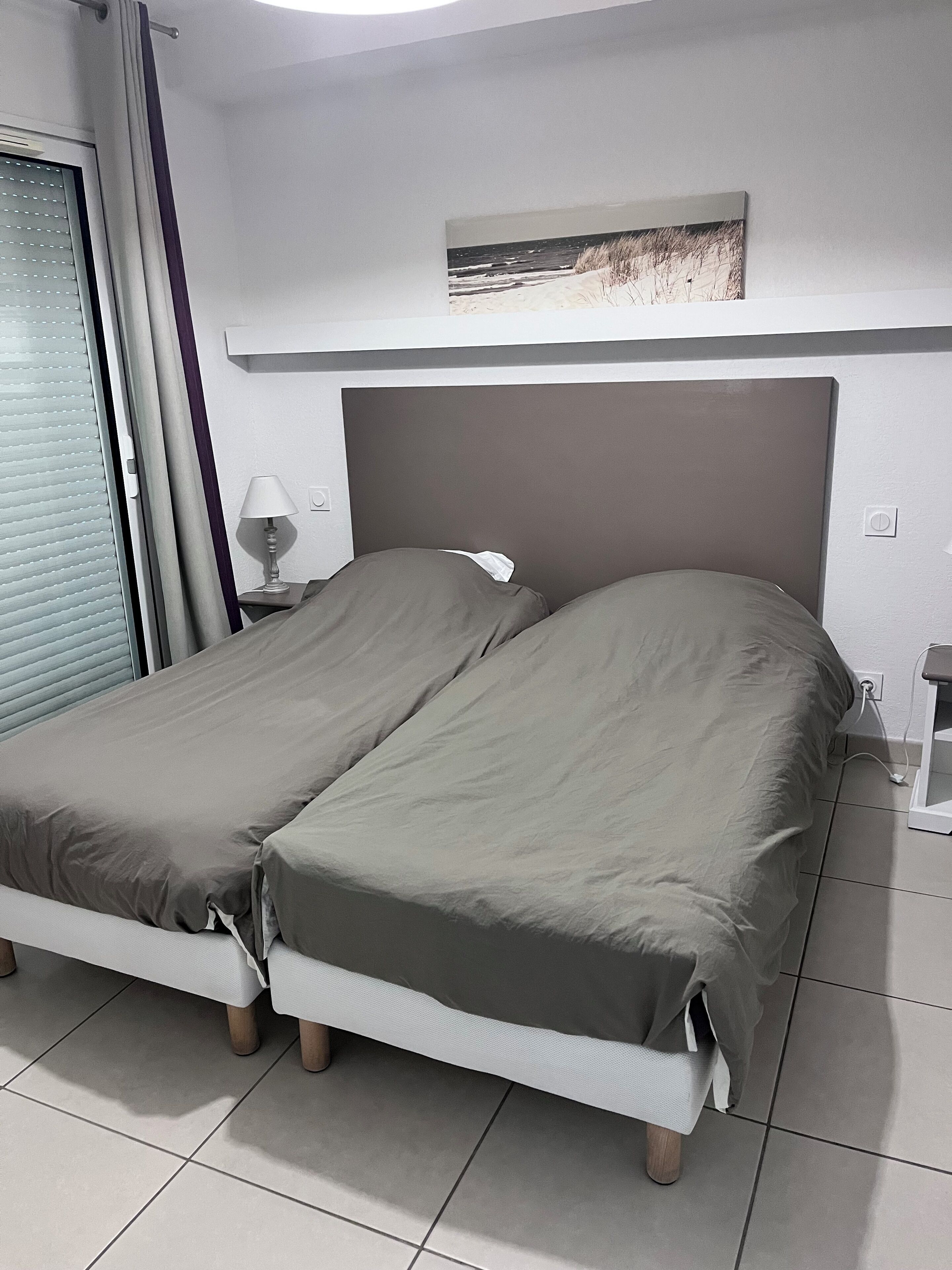 A double bed with a headboard, a bedside table with a lamp, and a wall-mounted picture.