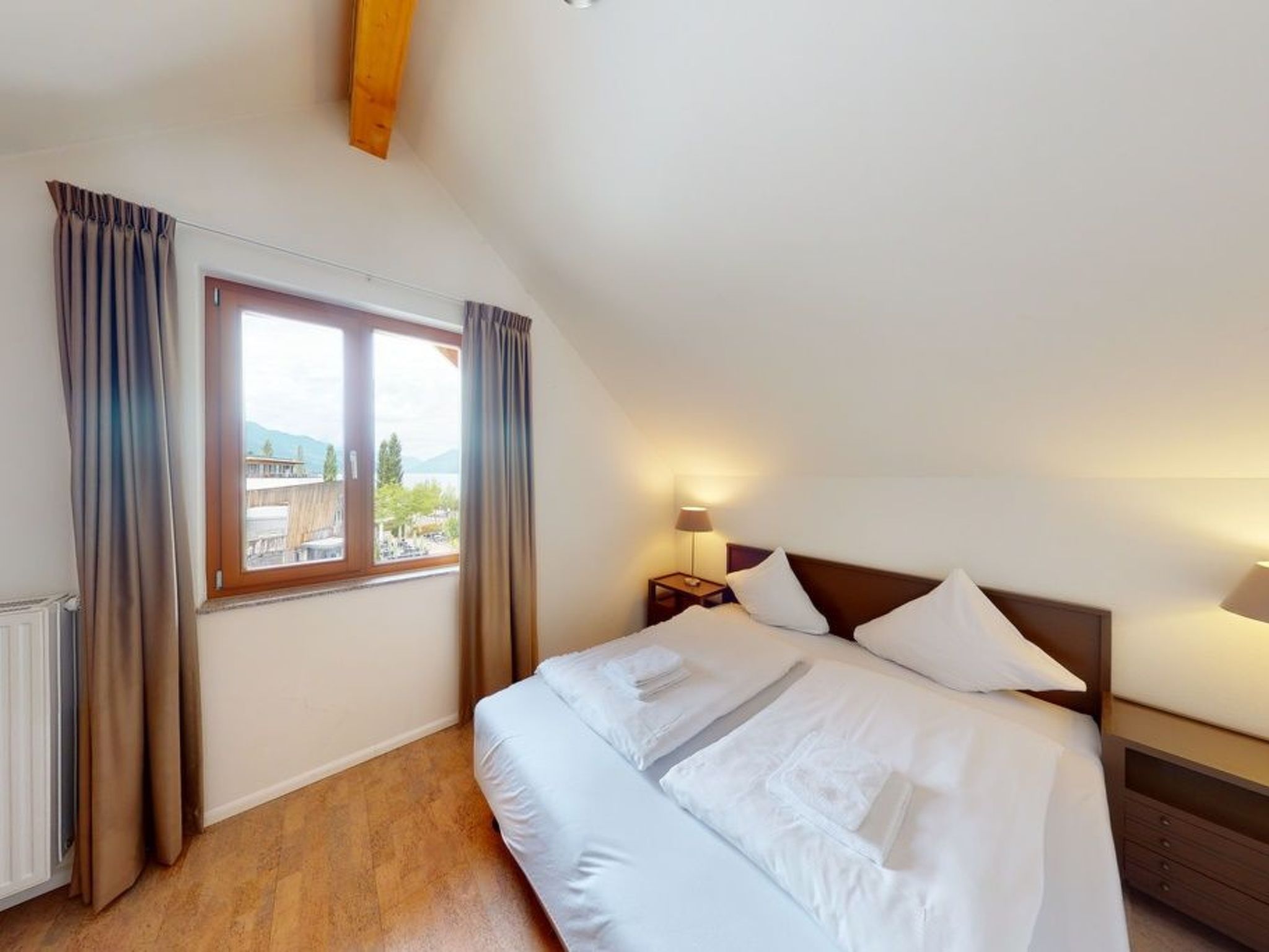 A hotel room with a large bed, a nightstand, a lamp, and a window with curtains.