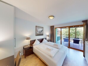 A hotel room with a large bed, a nightstand, a lamp, a painting, and a balcony with outdoor furniture. - Walensee House & Apartments, (Unterterzen), by Interhome (Unterterzen)