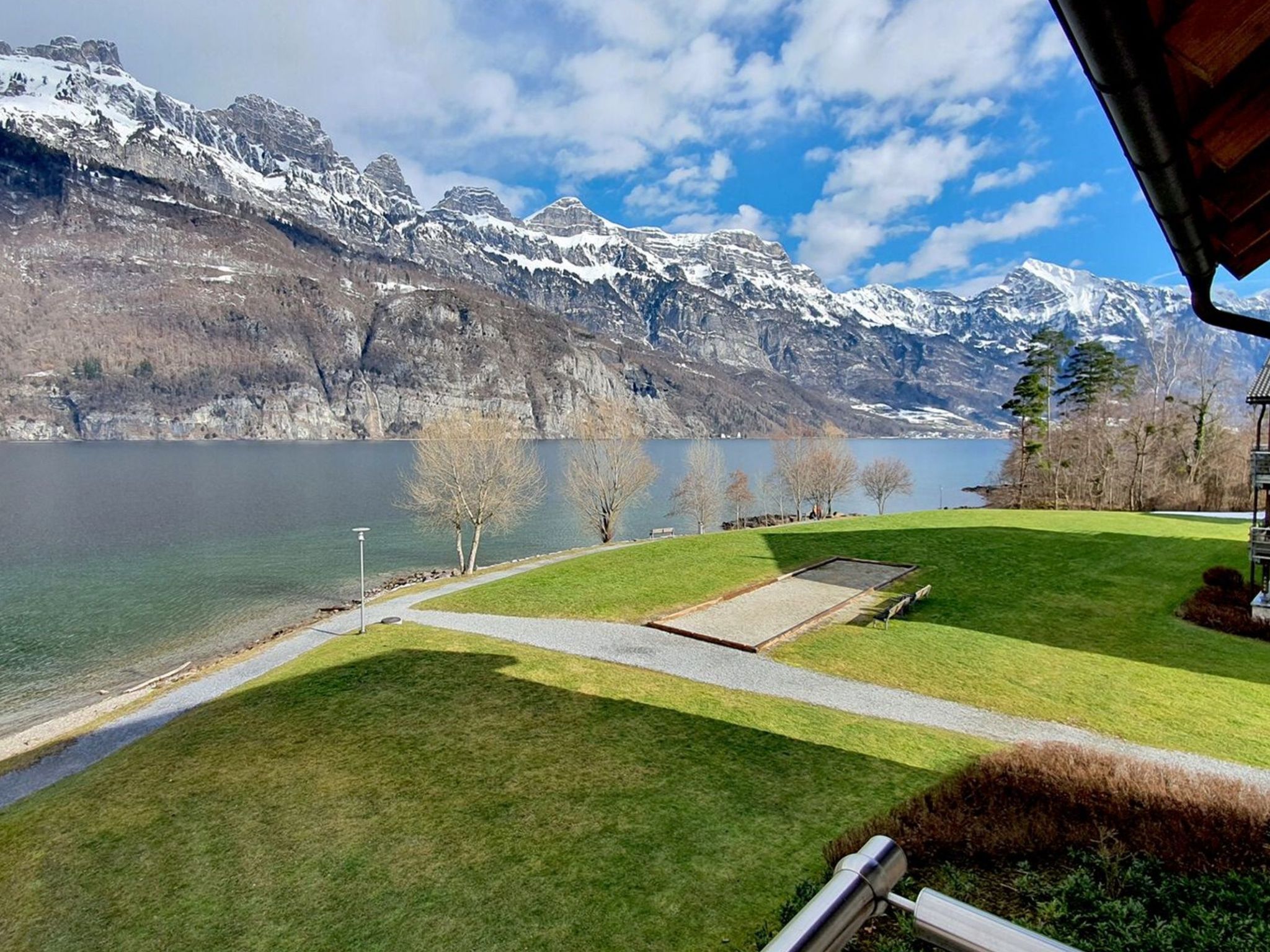 Vista del lago con zona verde, un sendero y un edificio de techo inclinado.