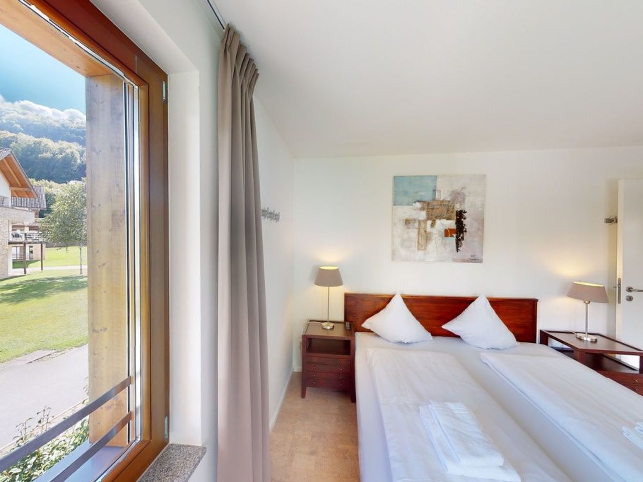Une chambre d’hôtel avec un lit, des tables de chevet, une lampe, un tableau au mur et une vue sur l’extérieur.