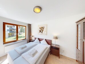 Ein Hotelzimmer mit zwei Betten, einem Fenster mit Blick auf Gebäude, einer Deckenleuchte, einem Nachttisch mit Lampe und einem Bild an der Wand.